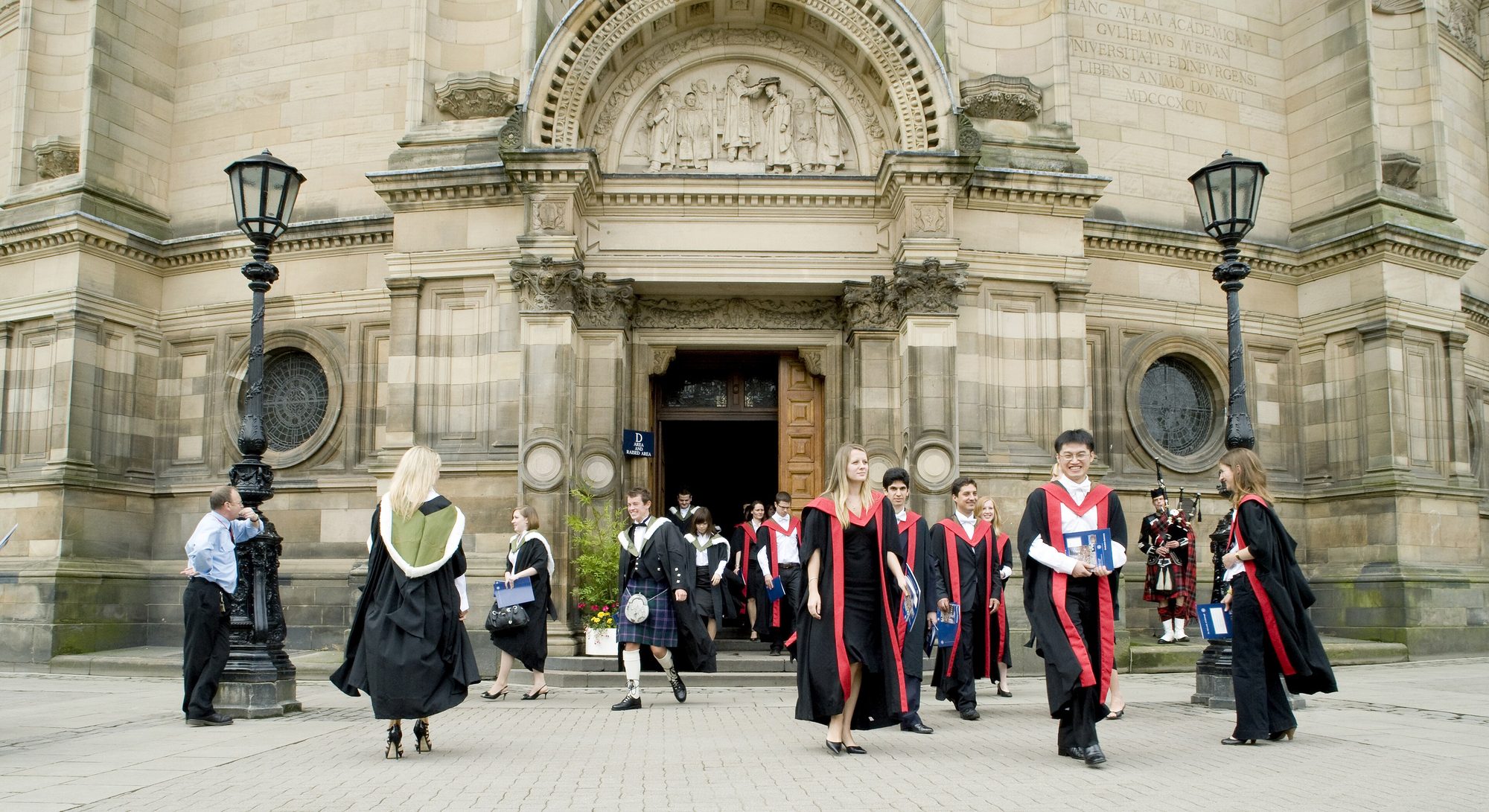 Graduates in gowns walking out of McEwan Hall, University of Edinburgh, led by a piper